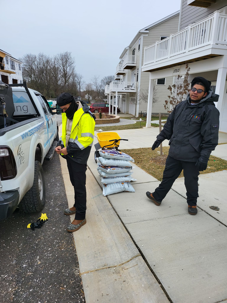 Two workers preparing de-icing salt bags and a spreader for American Snow Plowing Services in Rockville, MD.