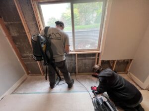 Workers removing damaged drywall and insulation near a window during water damage restoration by Utah Home Restoration in Springville, UT