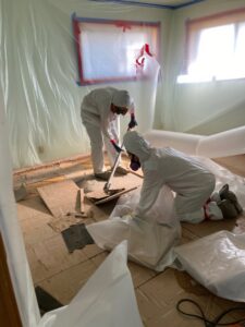 Two workers in hazmat suits removing damaged flooring in a contained area, a service by Central Oregon Disaster Restoration in Bend, OR.