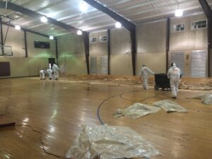 SERVPRO workers in protective suits removing damaged wooden flooring from a gymnasium, likely after significant water damage in Alexandria, LA.