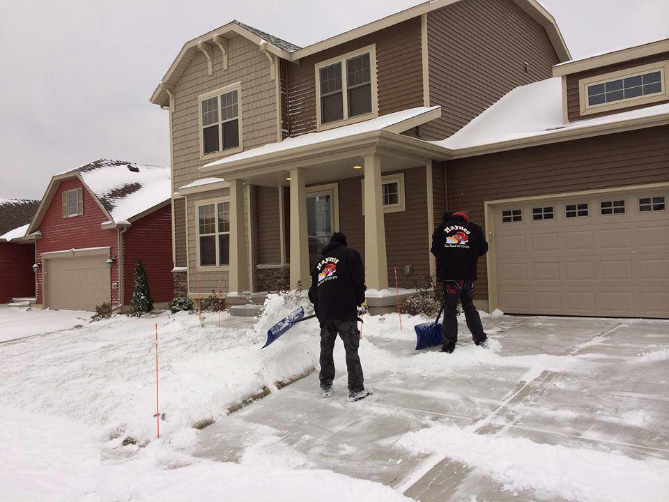 Two workers from Haynes Snow Removal & Lawn Maintenance shoveling snow from a residential driveway in Madison, WI.