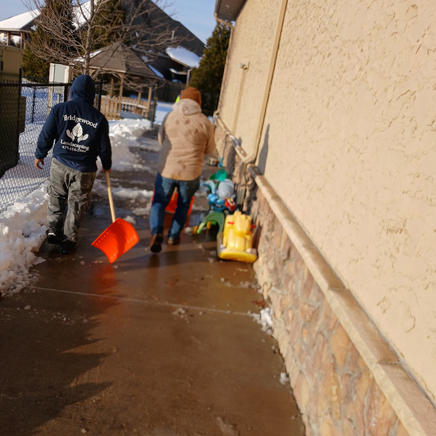 Two Bridgewood Landscape workers shoveling snow from a commercial sidewalk in Rogers, AR.