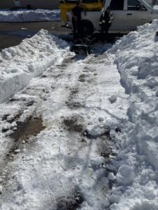 Two workers using a snow blower to clear a snowy path, with snow piled high, by Diamond Image in New Haven, CT.