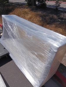 A large, wrapped couch on a dolly being moved outside by Rough Çutt Movers in San Diego, CA