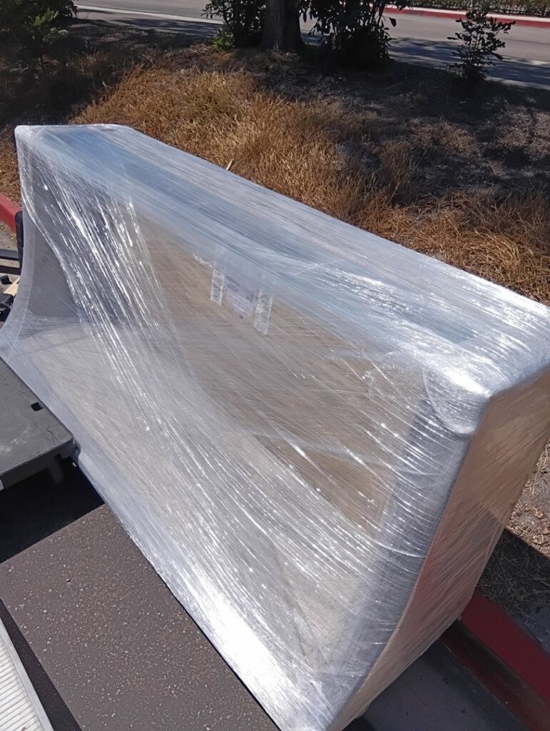 A large, wrapped couch on a dolly being moved outside by Rough Çutt Movers in San Diego, CA