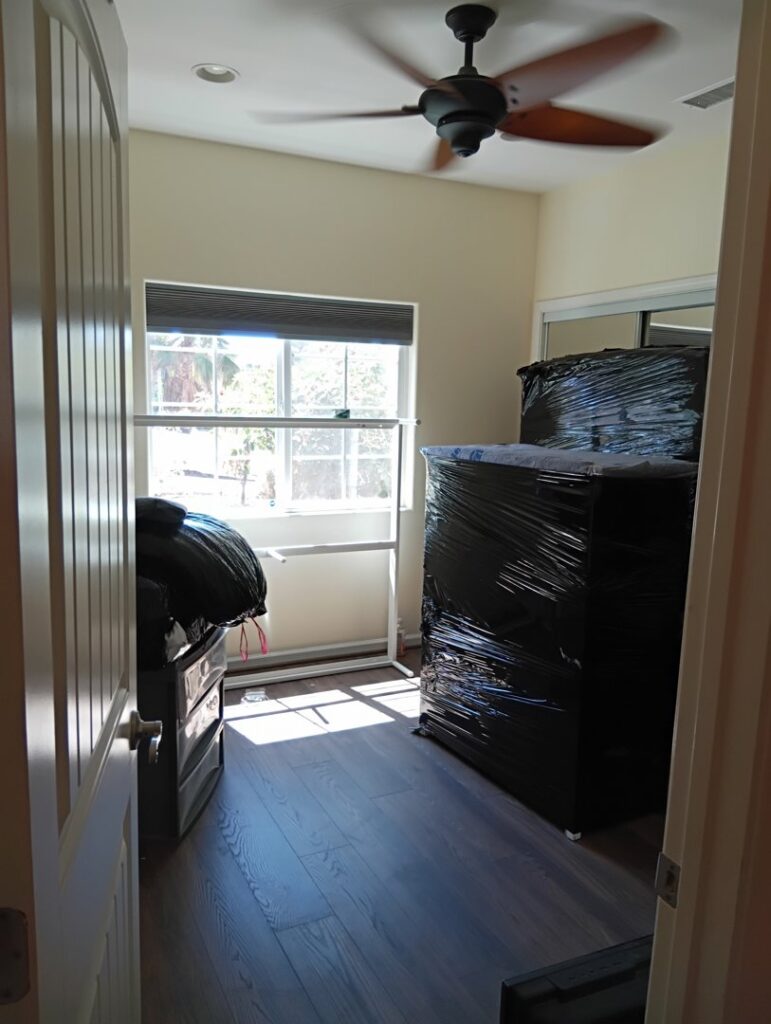 Several large pieces of furniture, wrapped in black plastic and on wheels, ready to be moved by Rough Çutt Movers in San Diego, CA.