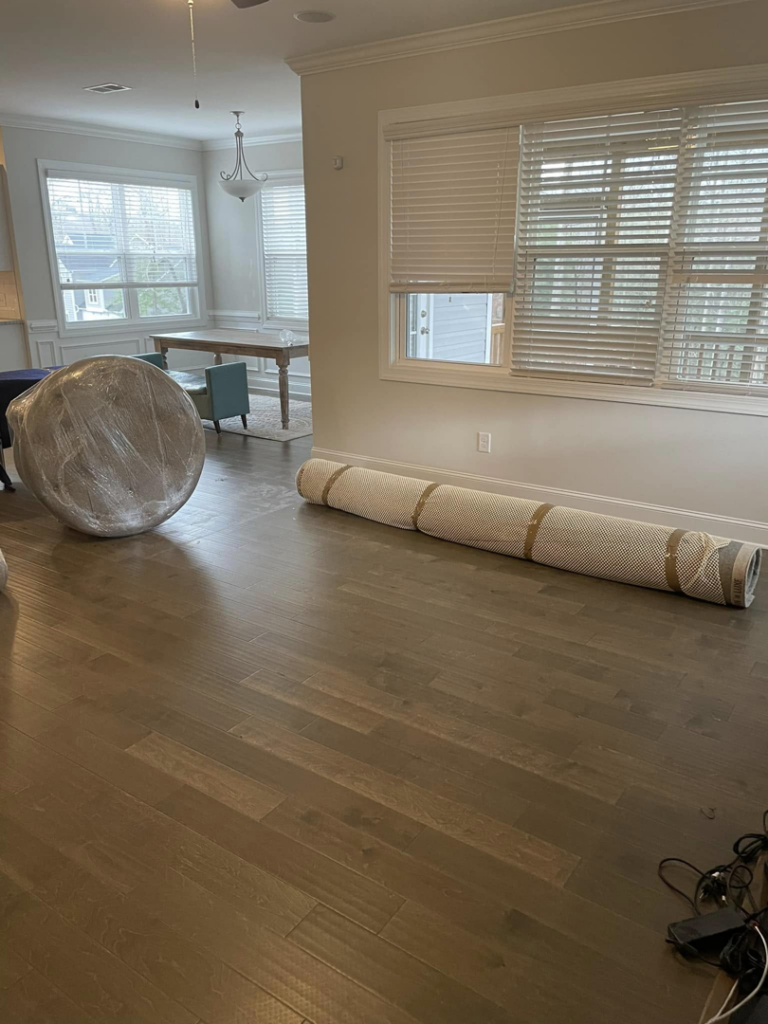 Wrapped furniture and a rolled rug in an empty living space, indicating a move by CNZ Moving in Raleigh, NC.