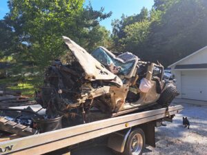 A completely wrecked Jeep being transported on a flatbed tow truck by Acme Towing Services in Greenville, SC.