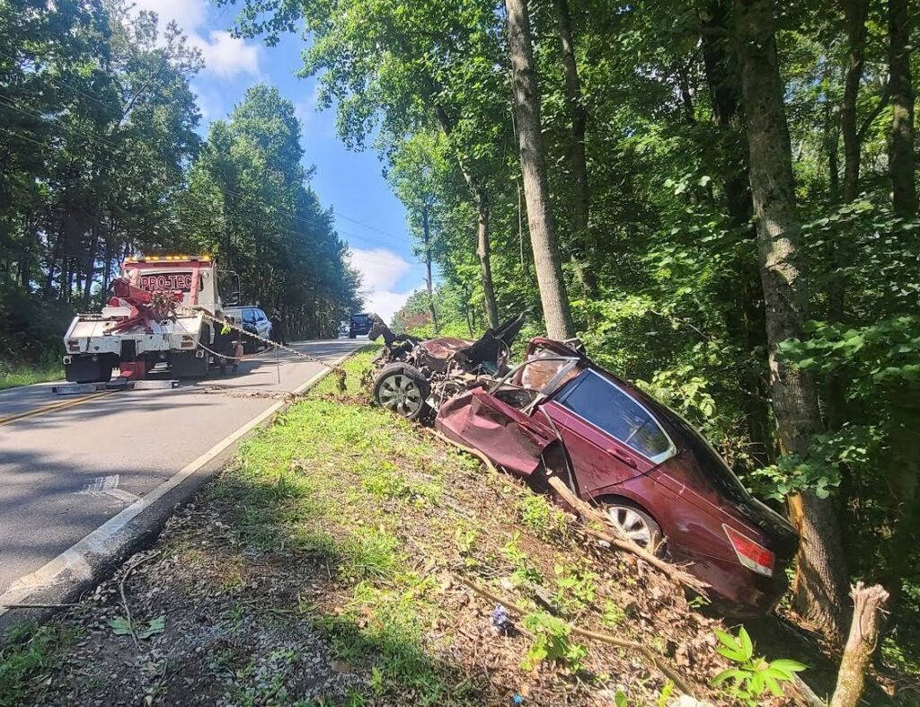 A Pro-Tech Wrecker Service tow truck at an accident scene with a heavily damaged car off the road in Decatur, AL.