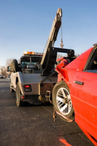 A wrecker tow truck recovering a heavily damaged red car after an accident for United Front Towing & Roadside in Nashville, TN