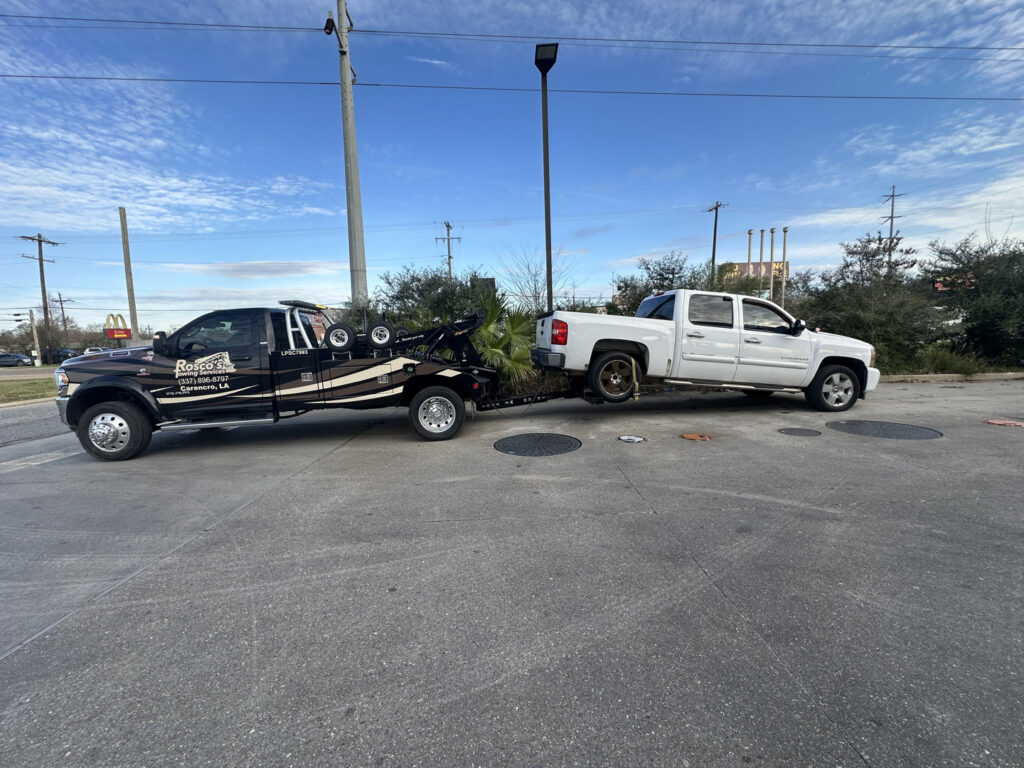 A wrecker tow truck from Rosco's Towing Services LLC towing a white pickup truck in Carencro, LA.