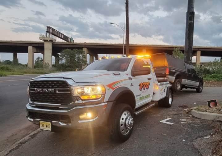 A Velez Towing wrecker truck towing a black SUV under a highway bridge in Newark, NJ.