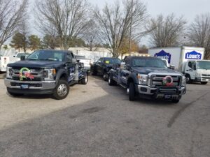 A Bobbys Towing & Recovery wrecker tow truck actively towing a car on the roadside in Raleigh, NC.