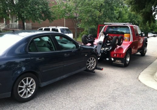 A wrecker tow truck from Raleigh Towing & Recovery towing a dark sedan with its front wheels lifted in Raleigh, NC.