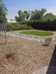 A xeriscaped backyard featuring a circular artificial grass area and river rock by SYNLawn of New Mexico in Albuquerque, NM.