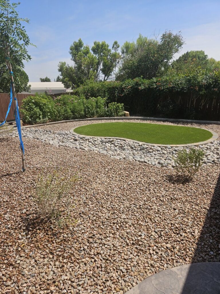 A xeriscaped backyard featuring a circular artificial grass area and river rock by SYNLawn of New Mexico in Albuquerque, NM.