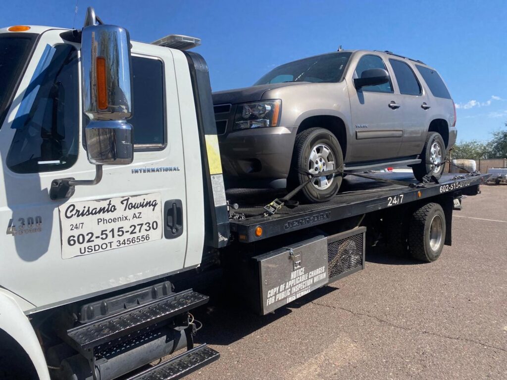 A yellow Chevrolet Camaro being transported on a flatbed tow truck by Crisanto Towing in Phoenix, AZ.