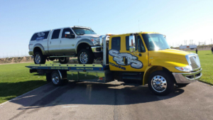 A yellow flatbed tow truck from SOS Towing carrying a silver pickup truck in Albuquerque, NM.