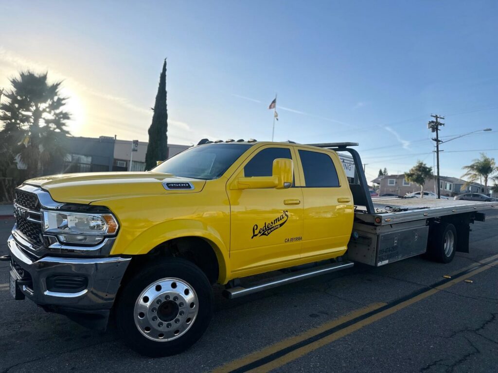 A bright yellow flatbed tow truck from Ledesma's Towing parked on a street in San Diego, CA.