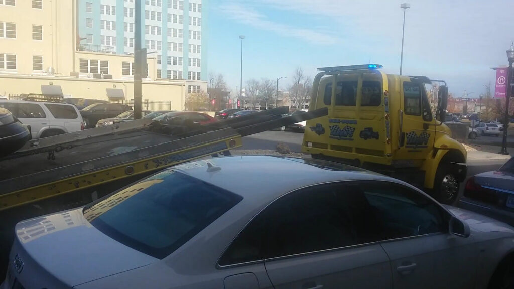 A yellow flatbed tow truck from Terry's Auto Service and Towing, LLC, loading a white car in Springfield, MO.