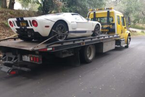 Aguilar Towing's yellow flatbed tow truck transporting a white Ford GT sports car in San Jose, CA