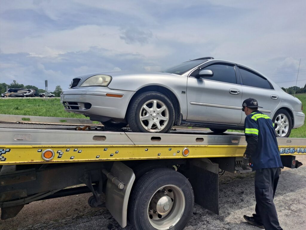 A yellow flatbed tow truck from Terry's Auto Service and Towing, LLC, towing a silver car in Springfield, MO.