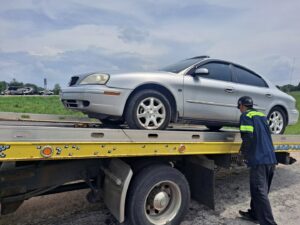 A yellow flatbed tow truck from Terry's Auto Service and Towing, LLC, towing a silver car in Springfield, MO.