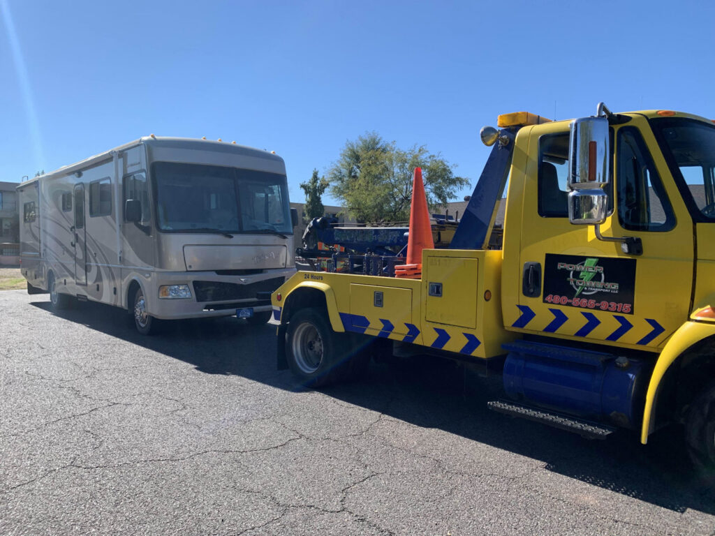 A yellow heavy-duty tow truck from Power Towing & Transport towing a large RV in Phoenix, AZ.