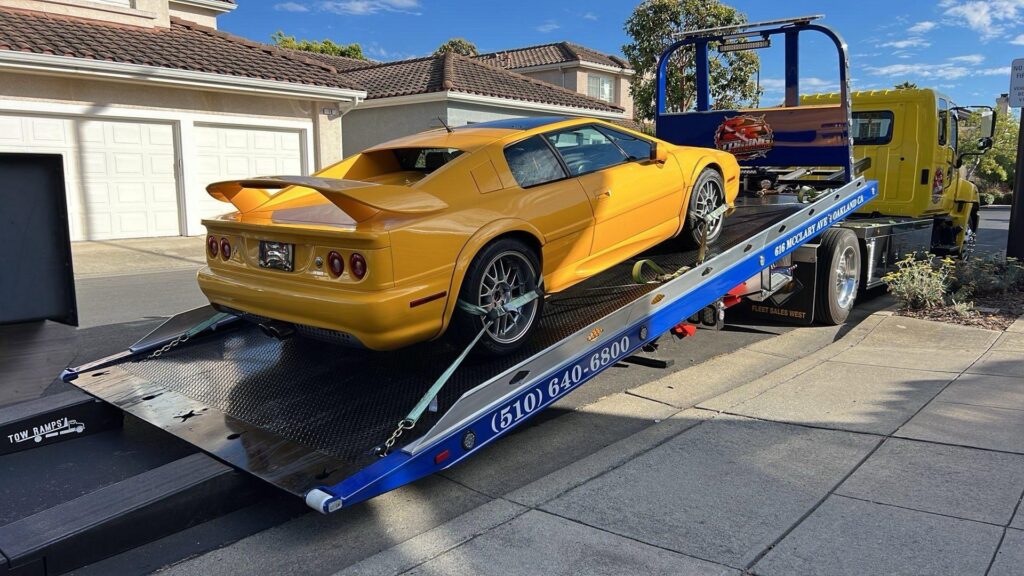 A yellow Lotus sports car is being loaded onto a flatbed tow truck by S&F Towing in Oakland, CA.