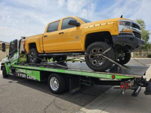 A yellow pickup truck being transported on a flatbed tow truck by Caliber Towing in Phoenix, AZ.