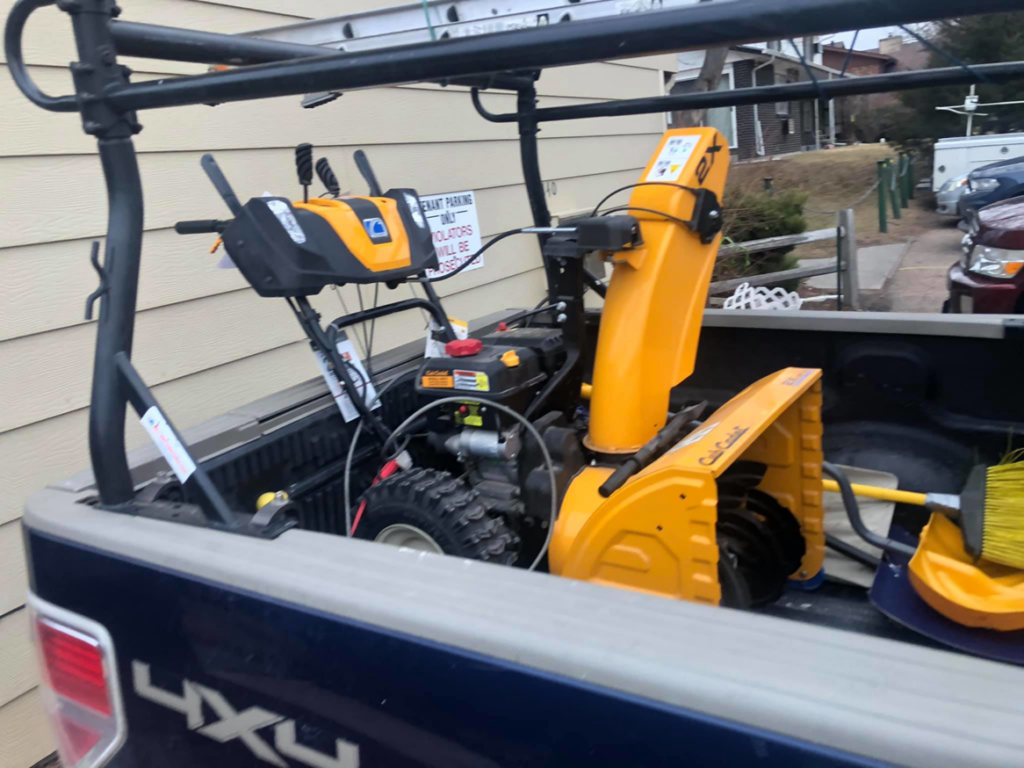 A yellow snow blower loaded in the back of a pickup truck, ready for snow removal by Elevated Legacy Solutions in Greeley, CO.