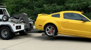 A yellow sports car being towed by a wheel-lift tow truck from Bakersfield Towing Company in Bakersfield, CA.