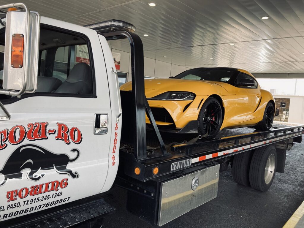 A yellow sports car being transported on a flatbed tow truck by Tow-Ro Towing in El Paso, TX.