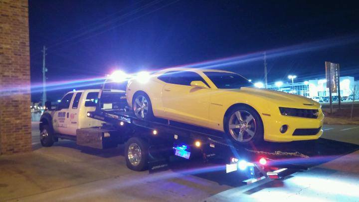A yellow sports car being towed on a flatbed tow truck by 918 Wrecker Service at night in Tulsa, OK.