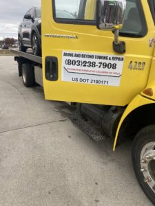 A yellow flatbed tow truck from Above and Beyond Headstones & Towing Services towing a dark SUV in Columbia, SC.