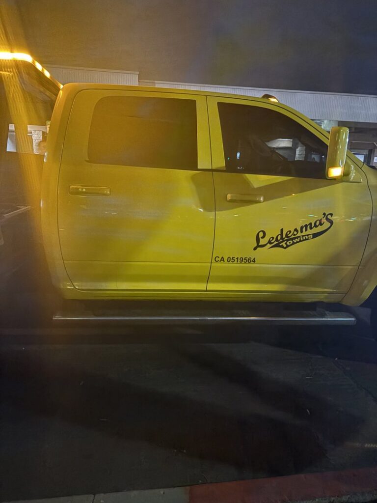 A yellow Ledesma's Towing truck with amber warning lights illuminated at night in San Diego, CA.