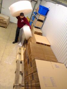 A mover from Your Friends - Moving Services carrying a large, round item in a warehouse in Lansing, MI.