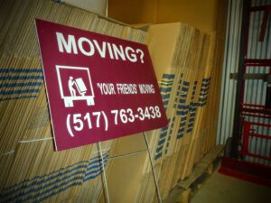 A 'Moving? Call Your Friends' sign in front of cardboard moving boxes from Your Friends - Moving Services in Lansing, MI.