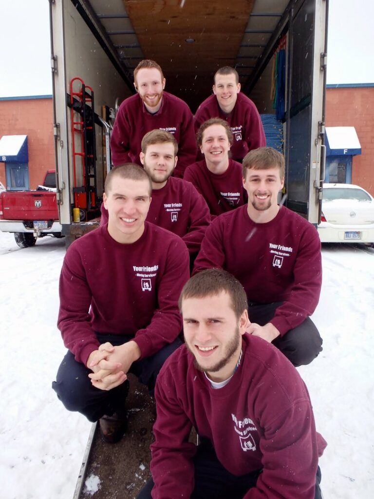 A team of 7 movers from Your Friends - Moving Services in maroon sweatshirts posing by their truck in Lansing, MI.