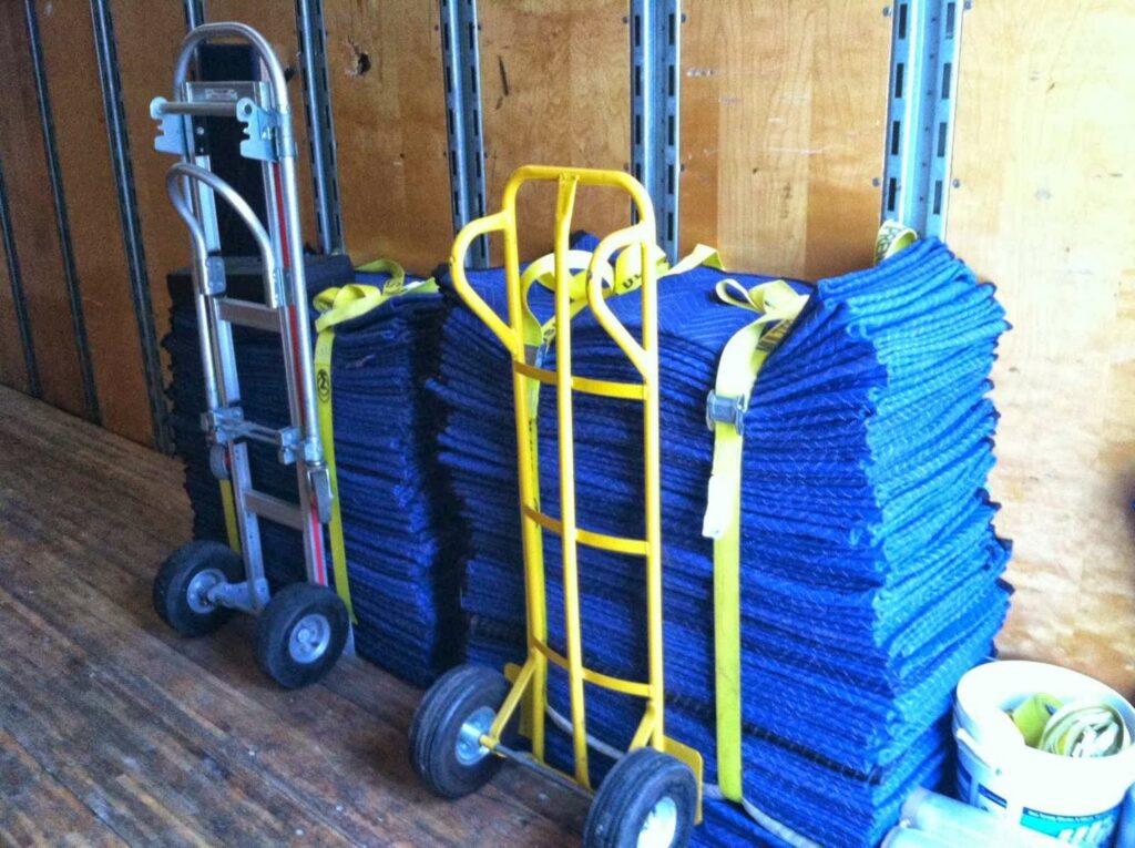 Hand trucks and stacks of blue moving blankets inside a Your Friends - Moving Services truck in Lansing, MI.